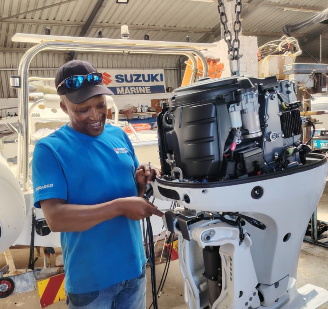 A Suzuki outboard motor being serviced by a mechanic in a well-equipped marine workshop